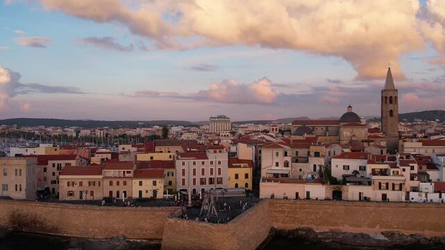 Aerial view of Alghero, Sardinia, showcasing its vibrant coastal scenery, historic buildings, and tranquil waters. Ideal for travel enthusiasts and explorers at sunset.