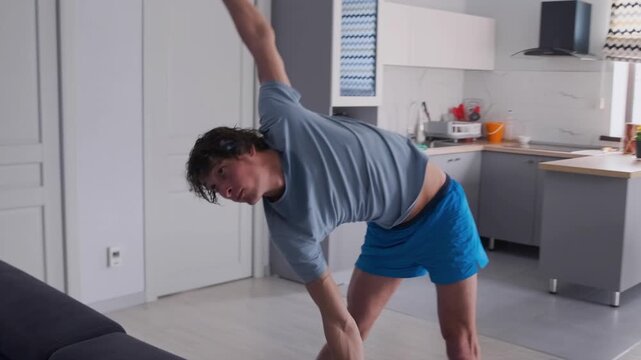 Caucasian man executing balance reach and stability drill on mat, hinge and reach motions, concentrated expression, household kitchen background, shorts and tee, training for coordination and