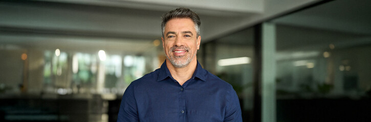 Headshot portrait of happy mature professional man of mid age standing in office. Smiling 50 years...