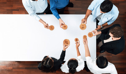 A diverse team engages in creative problem solving, collaboratively sharing gears on a modern white table, symbolizing innovation and teamwork in the workplace. Amity