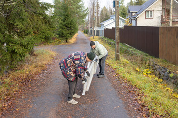 Two adult men using ladder at utility pole when replacing lamp on rural road surrounded by trees...