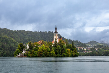 Bled Island has a church, trees, and water. It sits in the center of Lake Bled in Slovenia, creating a popular travel spot for visitors.