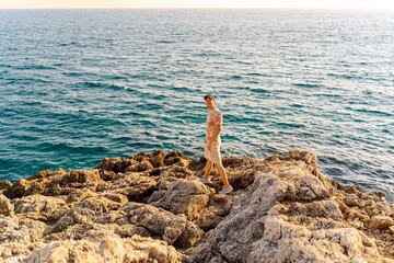 Young man walking on rocky seaside shore with ocean view during summer travel