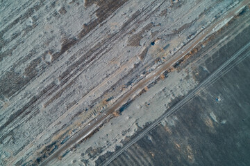 Diagonal country dirt road cutting through frozen winter field with dark soil and frost texture nature background top down aerial drone shot