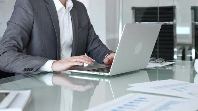 Businessman in suit typing on a laptop computer, working in a modern office setup, analyzing business documents and data. Business people concept