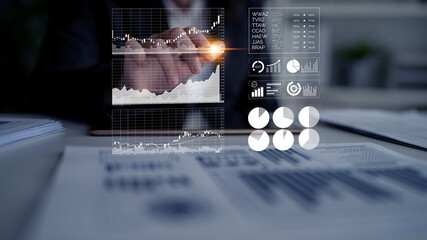 Businessman examines financial data using graphs and charts displayed on a virtual screen in a modern office, emphasizing technology in decision-making. Impute