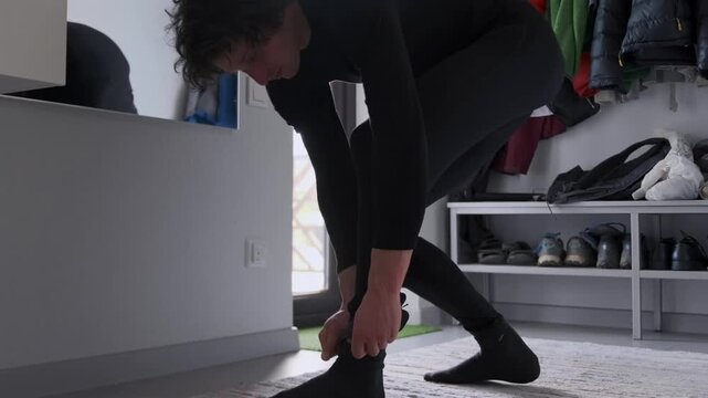 Caucasian man prepares footwear before jogging, Athletic young man readies shoes inside entryway at home, Young Caucasian male carefully adjusts socks and slips into trainers prior to workout