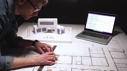Architects and engineers collaborating over cad on a laptop, paper blueprints and a 3d architectural model, reviewing plans and discussing design development at a desk