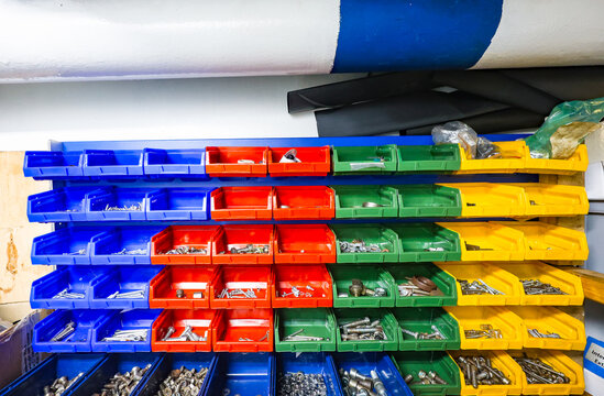 Colorful plastic storage bins with bolts, screws and metal fasteners organized on shelves in an industrial workshop or warehouse.