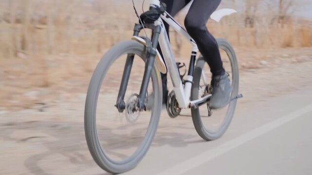 Closeup Cycling Pedal And Wheel With Steady Cadence And Focused Expression, Crisp Rim And Tire Detail, Puffer Jacket And Patterned Headband Visible, Smooth Road Contact And Deliberate Technique