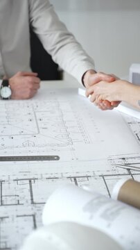 Handshaking between two architects finalizing a construction project deal, business partners agreeing on engineering blueprints and architectural models in an office, close up