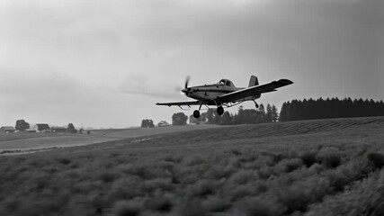 Agricultural crop duster plane flying low over a field from left to right as clouds cover the sky