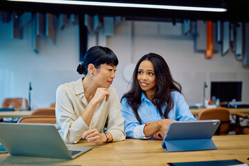 Two professional women discussing business ideas and tasks, sharing information on digital devices during an important office meeting