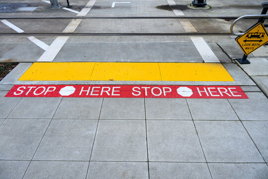 Pedestrian train tracks crossing, red making on sidewalk Stop Here and bright yellow tactile paving with truncated domes, ADA alert for caution, transportation background
