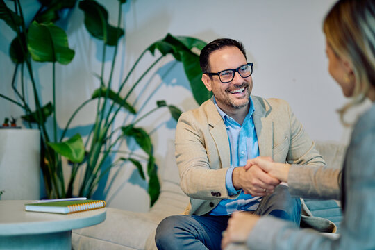Business man and woman shaking hands in a casual office setting, smiling, confirming a successful agreement and partnership