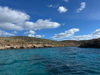 Calm turquoise sea with rocky coastline and blue sky.
Wide seascape with turquoise water, rocky shore and fluffy clouds, peaceful nature travel background