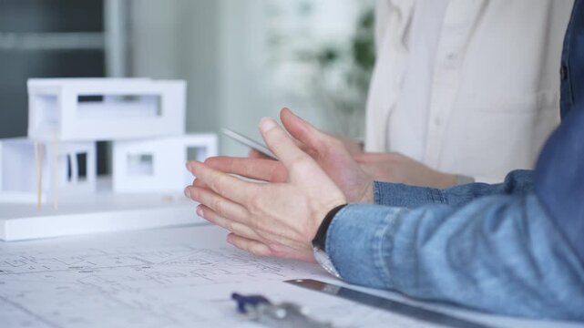Architects collaborating on blueprint plans, discussing engineering details and project designs, planning construction development with a laptop in a modern office environment