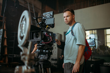 Director of photography with a camera in his hands on the set. Professional videographer at work on filming a movie, commercial or TV series. Filming process indoors, studio