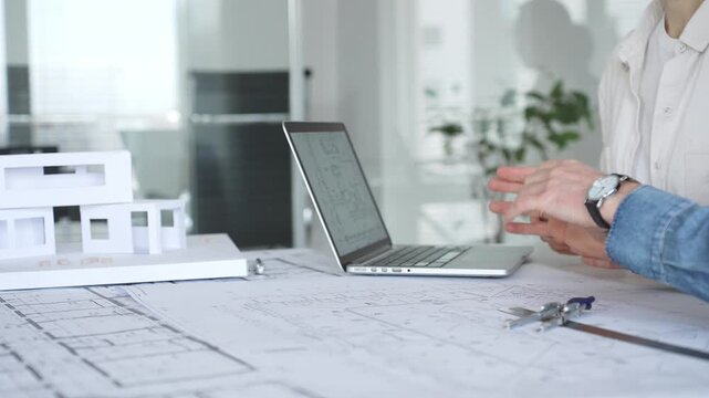 Architects collaborating over blueprints and a white scale model, using ruler and caliper on a shared desk as they plan residential and urban building projects