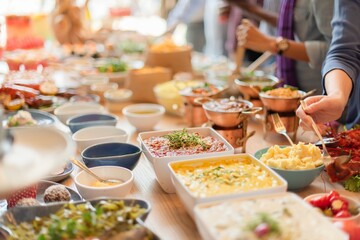 Obraz premium A buffet table with diverse dishes, including salads, sauces, and main courses. People serve themselves from the buffet, enjoying a variety of colorful foods. Buffet table with delicious food.
