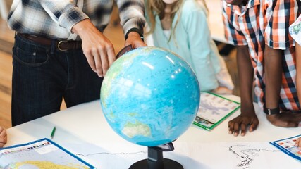 Diverse group of children exploring a globe. Kids learning geography, pointing at the globe. Educational activity with a globe, maps, and curious children. Students working together in class.