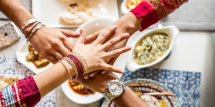 A vibrant gathering featuring diverse hands of South Asian women and men sharing a delicious meal. The joyful atmosphere highlights cultural unity and togetherness.