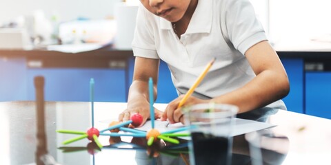 Child in a white shirt building a colorful molecular model in a science classroom. Focused on science, learning, and creativity with a molecular model. Education and knowledge concept.