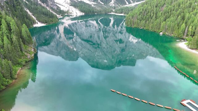 Vue a&eacute;rienne cin&eacute;matique du lac de Braies avec les reflets des montagnes des Dolomites et ses barques en bois