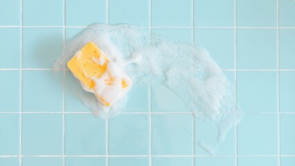 Yellow sponge with soap suds on light blue tiled backgrond. Sponge and soap create a clean, fresh...