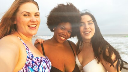 Three diverse women smiling at the beach, enjoying the sun and sea. Friends capturing joyful moments by the ocean, celebrating friendship and summer vibes. Diverse women at beach in summertime.