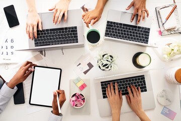 Top view of diverse group of hands collaboratively working on laptops and a tablet. Top view of teamwork's hands working together with laptop and tablet. Top view of business team working together
