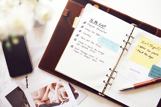 Flat lay photo of planner with to-do list, sticky notes, and pen. To-do list planner flat lay photo on working desk. Planner showing daily tasks and reminder notes, organizing daily to-do list