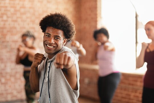 Smiling African American man in a fitness class, punching forward. The African American man is leading the class. Other participants follow the African American man's moves.