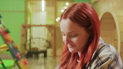 redhead white woman focused in creative studio sketching notes at table under warm string lights, wooden arches and green backdrop, calm expression, plaid shirt, freelance designer planning product