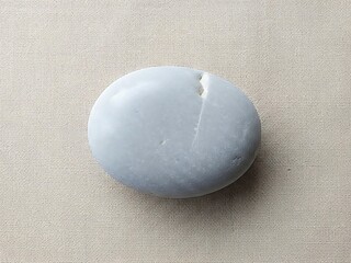 Smooth stone fragment on a beige textured surface, minimalist nature scene