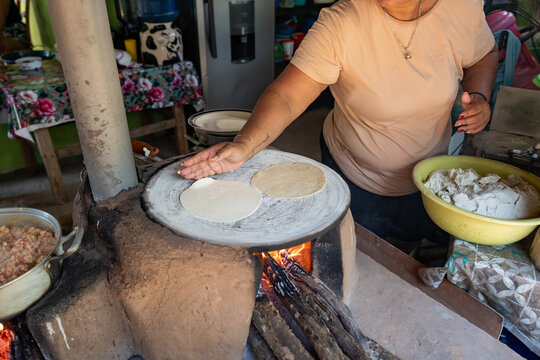 Mexican woman flipping tortillas on a traditional clay griddle (comal) over a wood fired stove. Artisanal Guerrero kitchen. Petatlan, Guerrero, Mexico