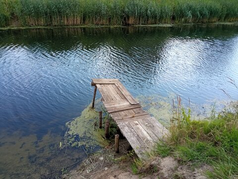 Small wooden pier on a river bank with reeds and quiet water