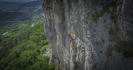 Woman lead climbing a vertical limestone cliff in the Osp climbing area, Slovenia. She is focused...