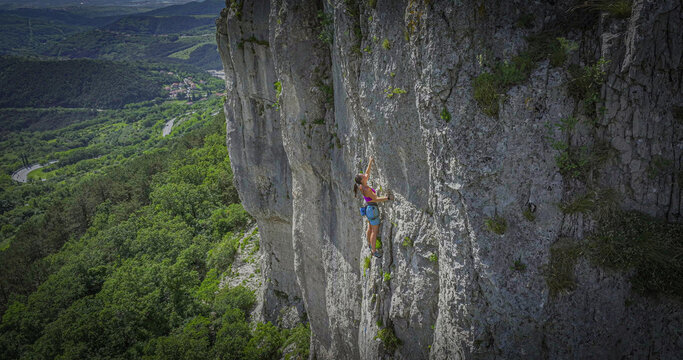Woman lead climbing a vertical limestone cliff in the Osp climbing area, Slovenia. She is focused while searching for her next hold. Authentic effort and skill required for outdoor rock climbing.