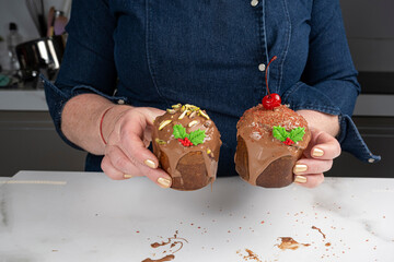 A pastry chef holding two small panettone cakes covered in melted chocolate.