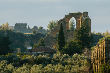 Historical ancient Roman ruins and stone arches of an aqueduct standing on a hill surrounded by olive trees and nature in Aspendos, Antalya region.