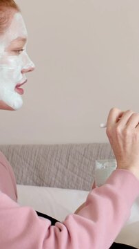 Vertical video: Handing brush and jar, friend applying mask to woman at home for skin wearing bands