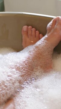 Vertical video: Flexing front foot, person's lower legs lifting in bathtub, bubbles and toe ring