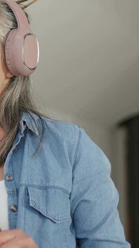 Vertical video: Putting on pink headset, woman prepping brushes in denim at home, copy space