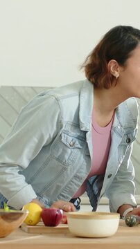 Vertical video: Leaning woman in denim jacket responding to cue and steadying herb jar in kitchen