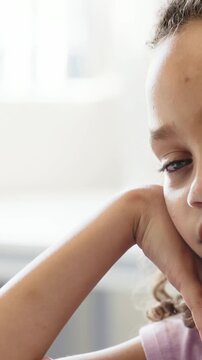 Vertical video: Starting child resting cheek on hand and arm waiting by window tee, copy space