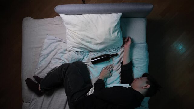 Man lying asleep in bed with an empty wine bottle next to him, depicting themes of addiction, loneliness, and despair from alcohol consumption, captured in a high angle view