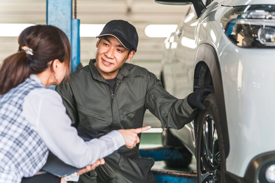 A male car mechanic and a female front desk clerk in business uniform talking in front of a car