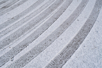 Snow-covered road with visible tire tracks forming repeating diagonal patterns. Winter texture background illustrating cold weather, icy driving conditions, and seasonal transportation challenges