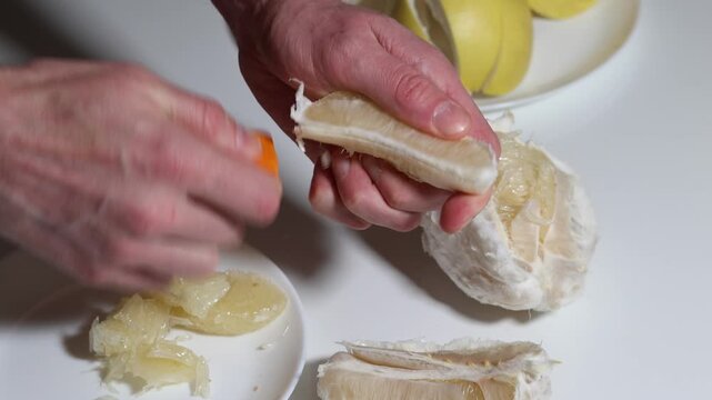Close up of hands peeling a pomelo segment with an orange peeler, revealing its juicy pulp and ripe segments, demonstrating a healthy lifestyle choice and fresh citrus fruit preparation